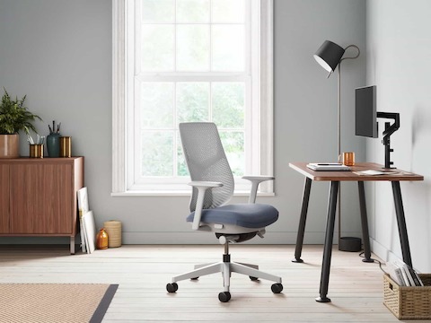 Una seduta Verus bianca con sedile azzurro vicina a una scrivania Memo con piano in noce accanto a una finestra, con una unità di archiviazione Sideboard di naughtone sull sfondo.