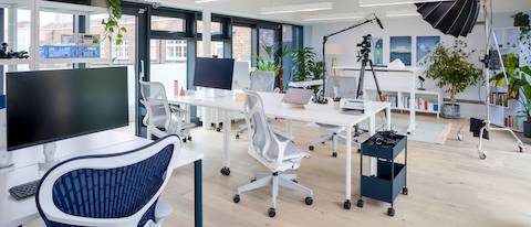 Table blanche mobile OE1 avec un siège Cosm mid-dos et un bureau à hauteur réglable Ratio dans le fond.