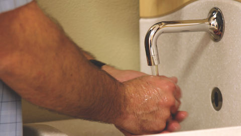 A physician washes his hands at a sink inside of a medical area. 