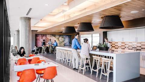 Office employees converse and work in an open environment with abundant natural light. 