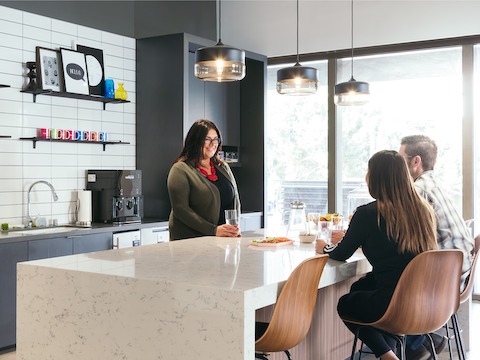A man and a woman sitting at a counter socializing with a woman across from them in a kitchen. 