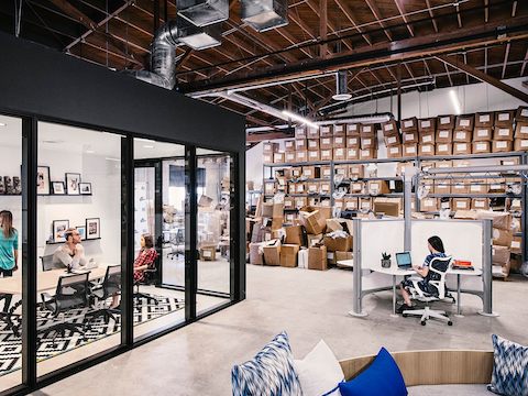 Office employees work at their desk and in a conference room with boxes in the background.