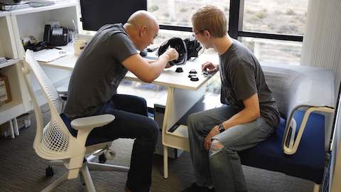 Two people examine a piece of virtual reality equipment together. 