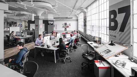 Employees work at their desks inside of an open office space while seated in Aeron chairs. 