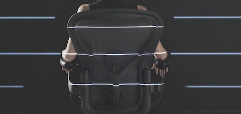 A rear view of a person sitting in an Aeron chair. 