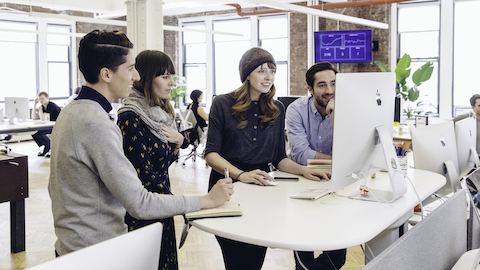 Two women and two men gather round a standing-height table to view a computer monitor.