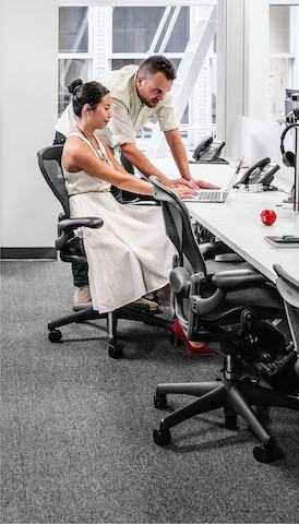 Ein Mann und eine Frau sehen eine Laptop-Computer in einer Bankeinstellung an, die schwarze Aeron Bürostühle kennzeichnet.