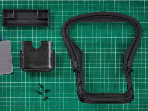Overhead view of a black Aeron back frame and Aeron Tilt cover, a line of fanned Revenio textile color swatches and several bolts arranged across a green table top.