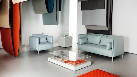 Blue ColourForm seating beneath hanging textiles of various colors. Select to go to an article about an exhibit featuring designers Scholten & Baijings.