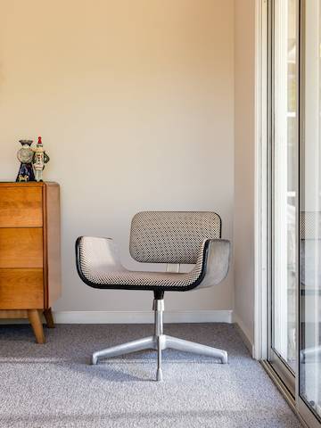 A single black and white upholstered chair with metal legs sits in a corner of a room, next to sliding doors and a small wooden dresser.