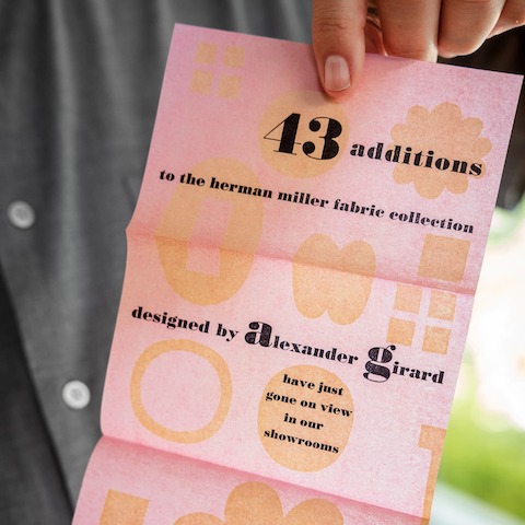 A light pink paper invitation with orange shapes and black text.