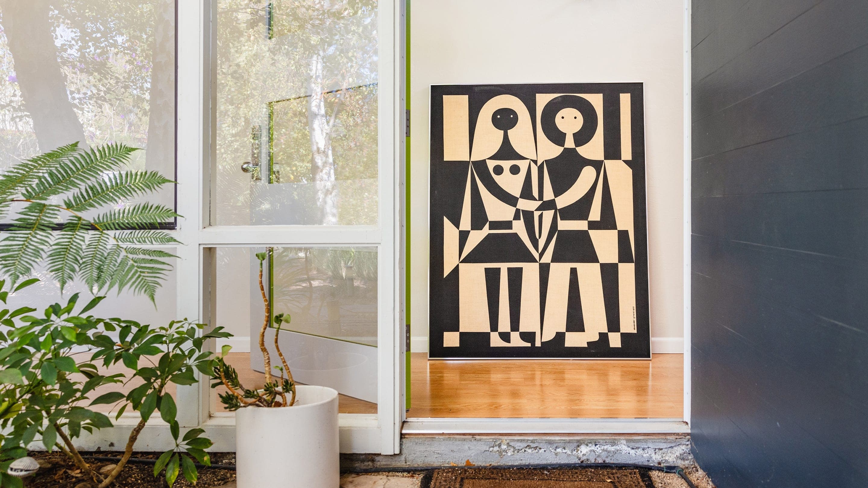 A bold black and white textile graphic of a man and woman is framed through modern windows and plants.