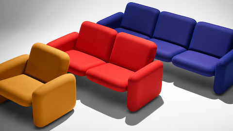 A yellow Wilkes Modular Sofa Group Chair, a red Wilkes Modular 2 Seat Sofa and a blue Wilkes Modular 3 Seat Sofa each placed in front of each other angled in a line.