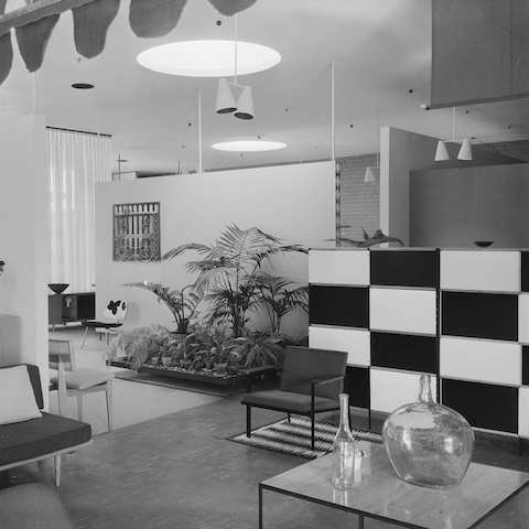 Two black and white archival photos of the Herman Miller Los Angeles showroom, designed by Eames Office, featuring Eames Shell Chairs and an Elliptical Table. 