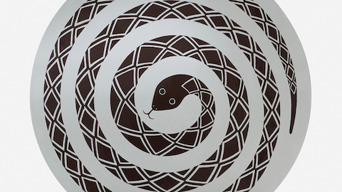 Overhead view of a round occasional table bearing the image of a coiled snake. Select to go to an article about misfit Herman Miller designs.